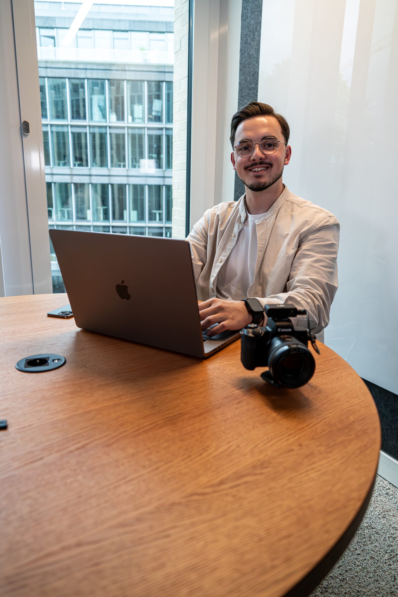 Eren Çiçek an seinem Schreibtisch mit MacBook und Canon-Kamera, lächelnd
