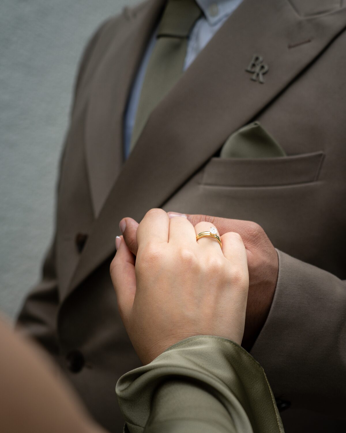 Brautpaar Hand in Hand, Bräutigam im braunen Anzug mit Anstecker, goldener Ring der Braut